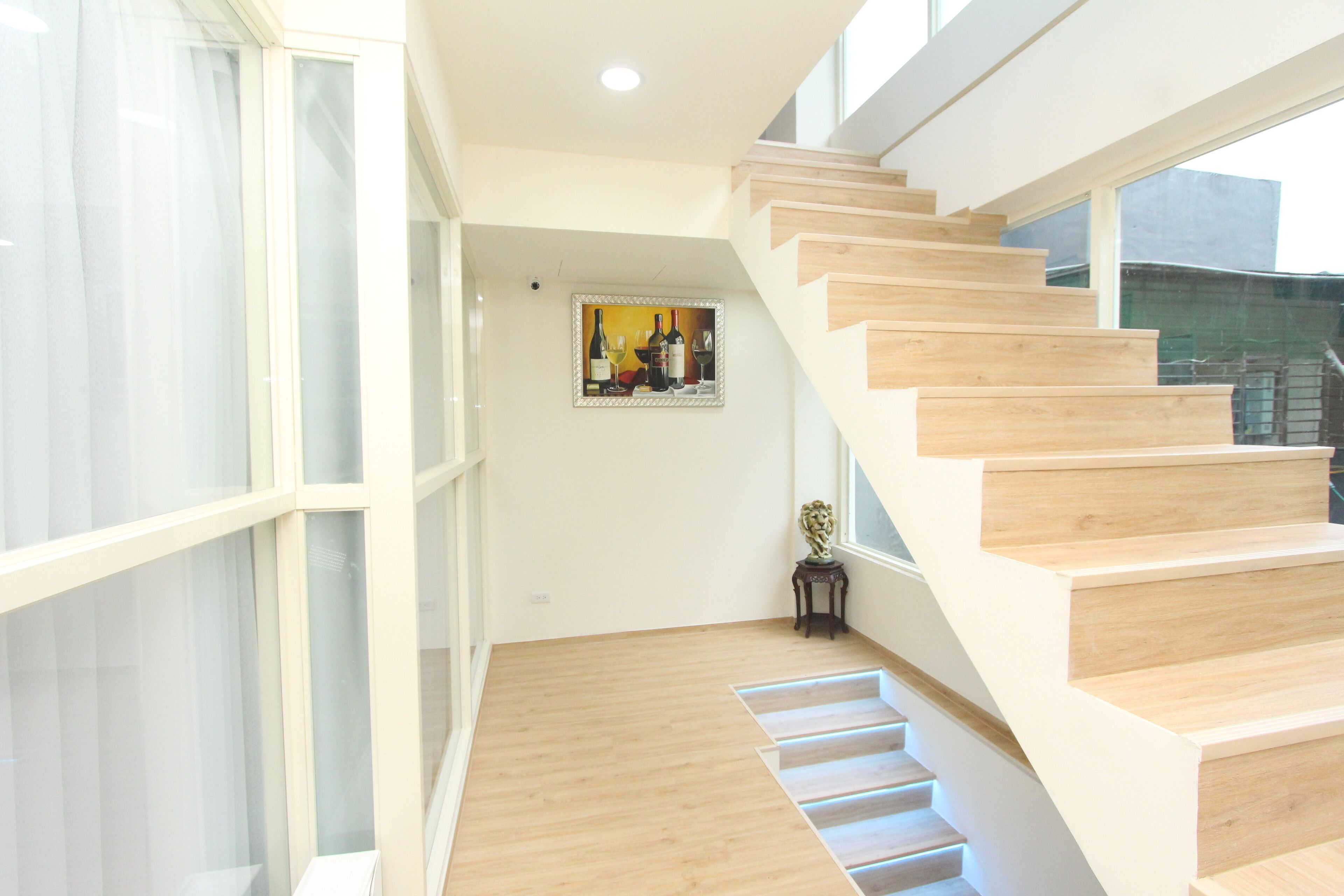 A modern staircase with wooden steps and a glass railing, leading to a room with a large window and a framed artwork on the wall.