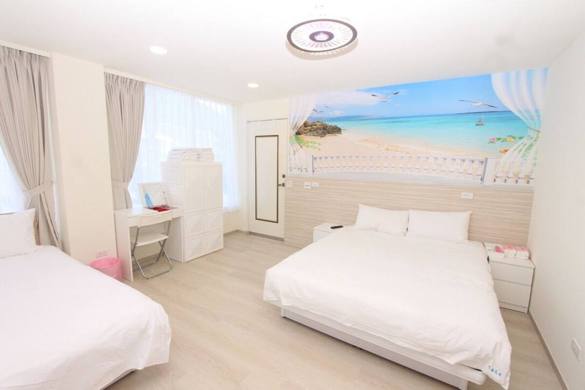 Une chambre d’hôtel avec deux lits, un bureau et une fresque représentant une plage sur le mur.