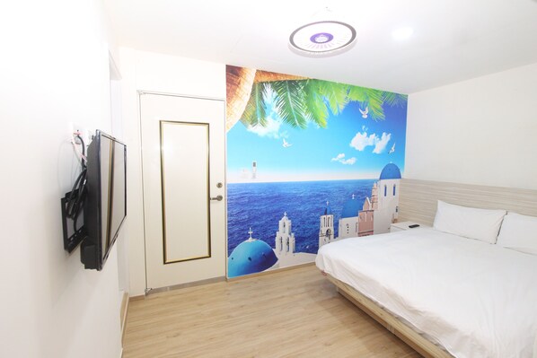 Une chambre d’hôtel avec un lit, un téléviseur fixé au mur et une fresque représentant un paysage côtier.