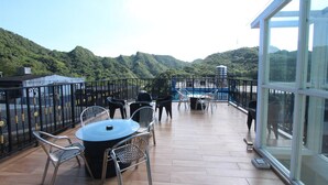 Una terraza con una mesa redonda y sillas, barandilla de cristal y vistas a colinas verdes.