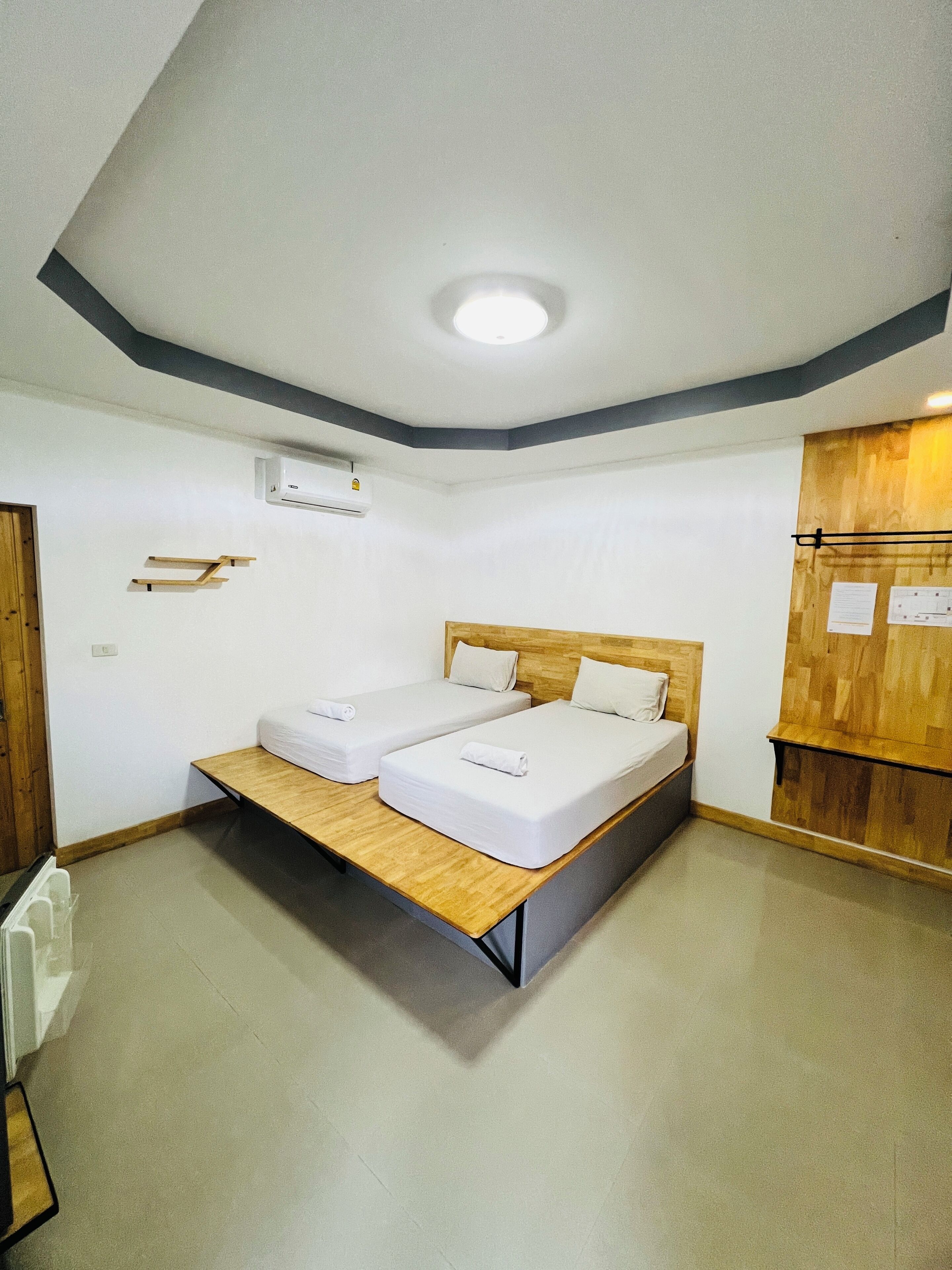 A room with a bed, a wooden bench, an air conditioning unit, and a bulletin board.