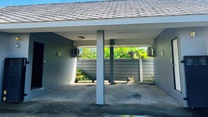 A covered outdoor area with a tiled roof, concrete floor, and a door leading to a building. - Phatra Resort (Saraburi)