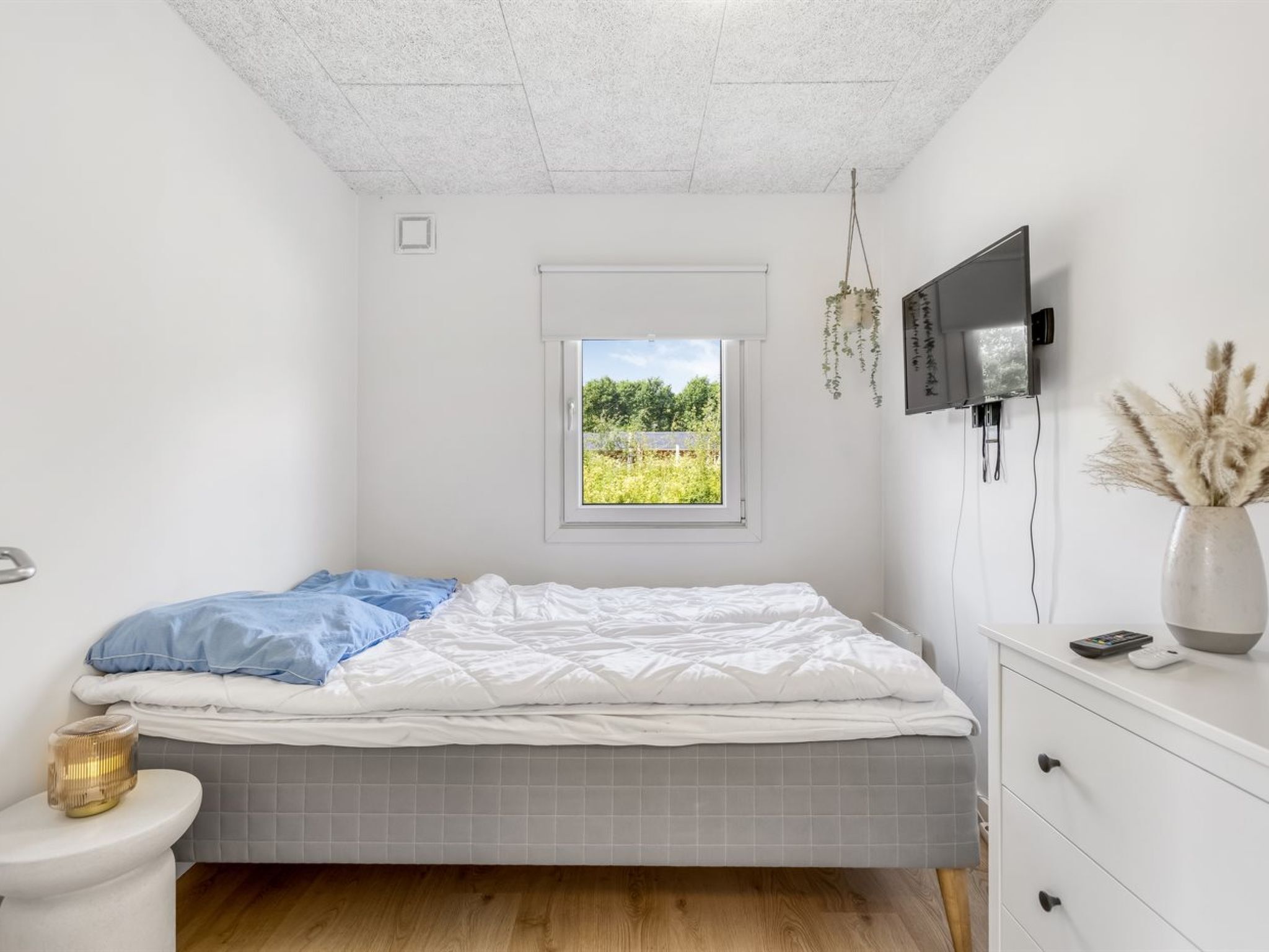 A bedroom with a bed, a window, a TV, a vase, and a bedside table.