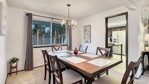 A dining area with a wooden table, six chairs, and a chandelier. - Entire home in Port Orchard, Washington with Game Room, Fire Pit and RV Parking (Port Orchard)