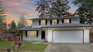 A two-story house with a garage, surrounded by a well-maintained lawn and flowering plants. - Entire home in Port Orchard, Washington with Game Room, Fire Pit and RV Parking (Port Orchard)