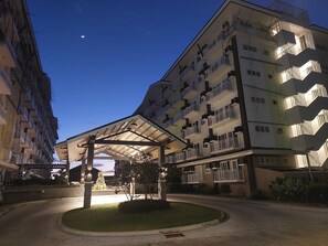 A multi-story residential building with balconies, a covered entrance, and a well-maintained lawn. - Cozy Condo Near Airport with Pool and Gym (Lapu-Lapu City)