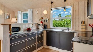 A modern kitchen with wooden paneling, a large window, and a view of greenery.