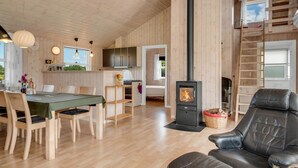A cozy cabin interior with a dining area, a black leather sofa, a wood-burning stove, and a loft bedroom with a view.
