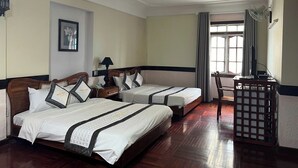 Habitación de hotel con dos camas, un escritorio, una silla, un ventanal con cortinas y un cuadro en la pared.