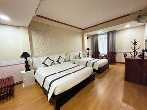 A hotel room with two beds, a desk, a chair, a lamp, and a window with curtains. - Orient Hotel Da Nang (Da Nang)