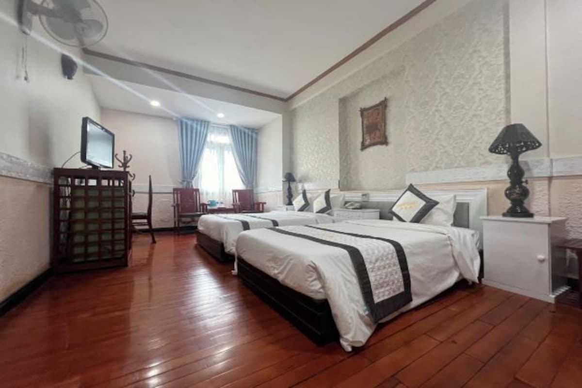 A hotel room with two beds, a desk, a chair, a small table, and a lamp.