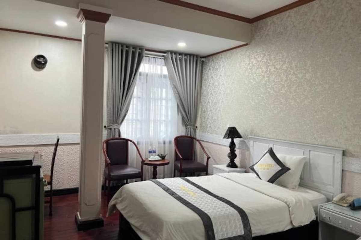 A hotel room with a bed, two chairs, a small table, a lamp, and a nightstand.