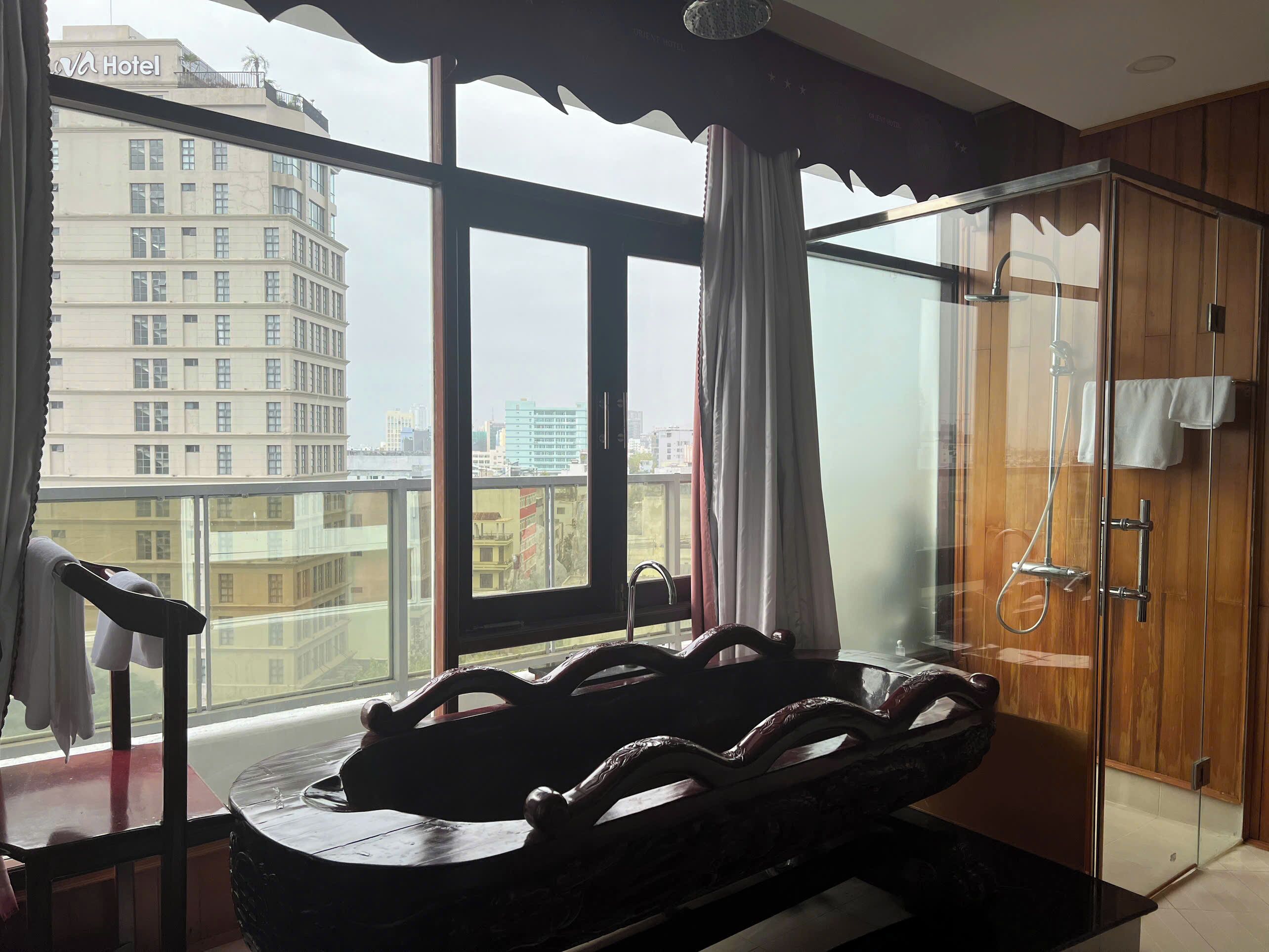 A hotel room with a large window, a wooden cabinet, and a shower area.
