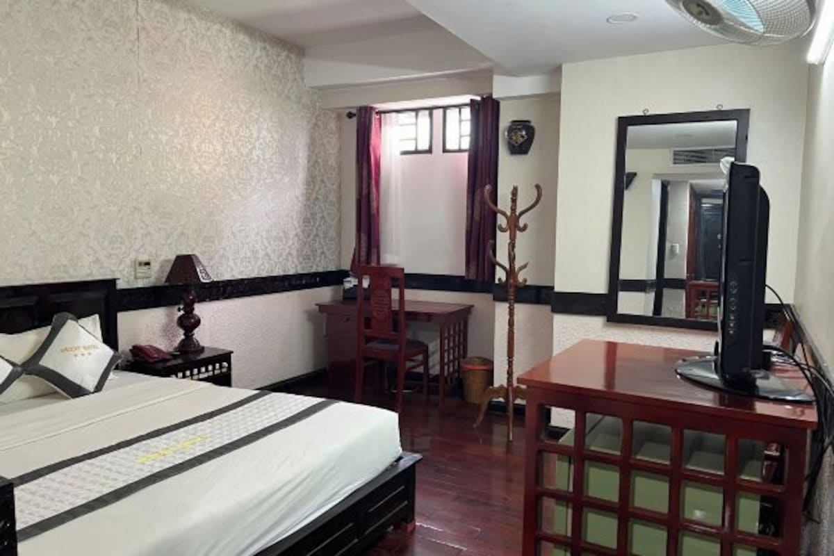 A hotel room with a bed, a desk, a chair, a TV, and a mirror.