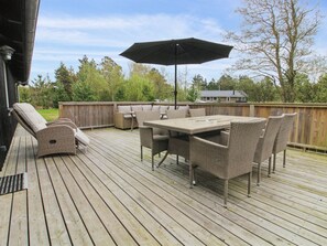 Une terrasse en bois avec des meubles d’extérieur, notamment une table et des chaises, ainsi qu’un grand parasol.
