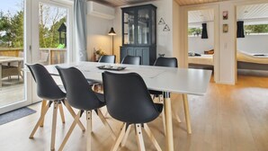 Un espace repas moderne avec une table blanche, des chaises noires et un plafond en bois.