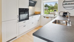 Une cuisine moderne avec des meubles blancs, un four noir, une grande fenêtre et une vue sur l’extérieur.