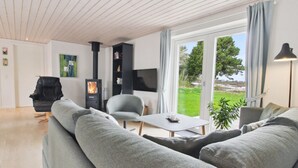 Un salon moderne comprenant un canapé, un fauteuil, une table, un téléviseur, une cheminée et une vue sur l’extérieur.