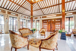 A spacious lobby with high ceilings, large windows, and traditional wooden furniture. - Capital O 93994 Dalem Kamulyan Syariah Guest House (Pakem)