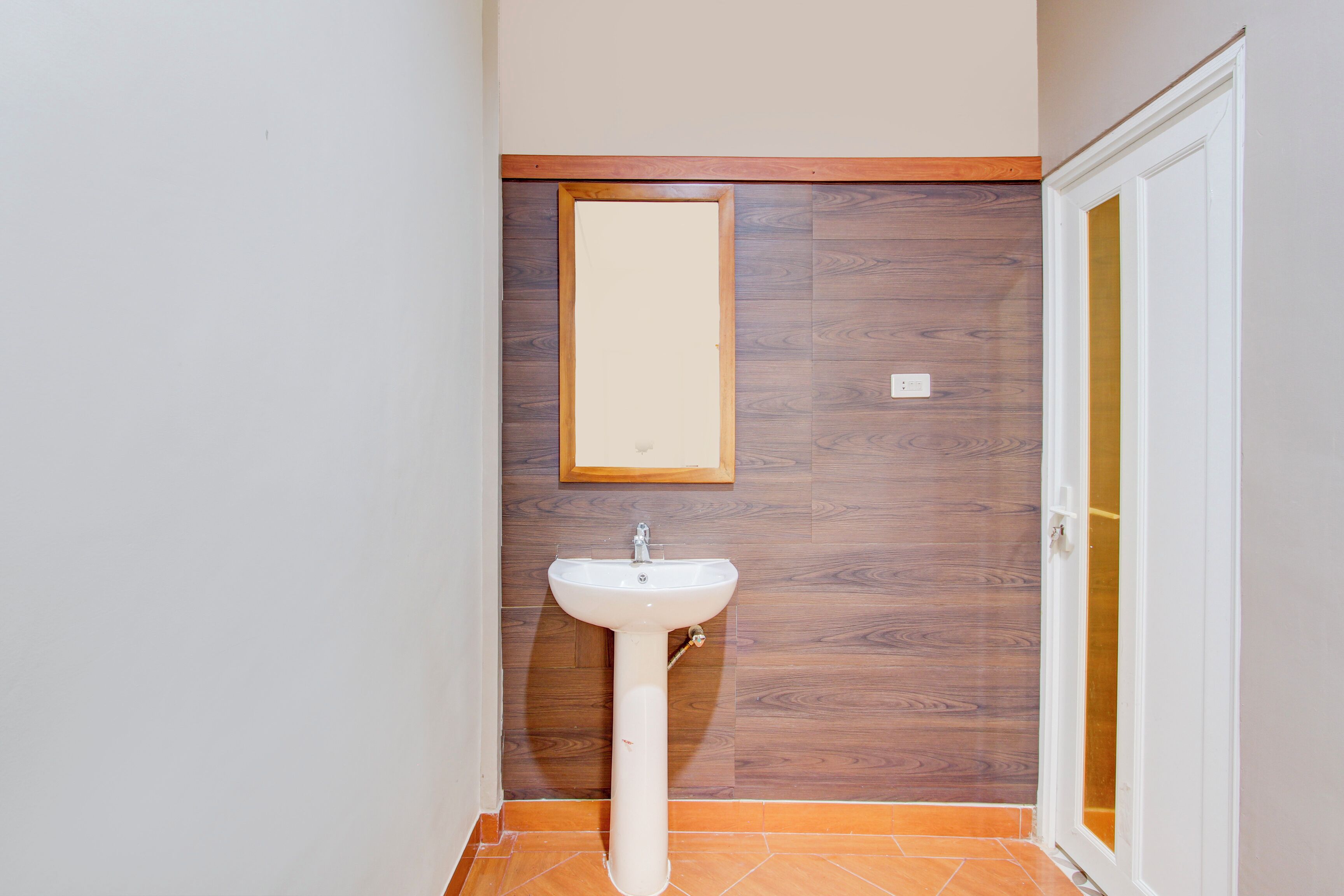 A bathroom with a white pedestal sink, wooden wall paneling, and a framed mirror.