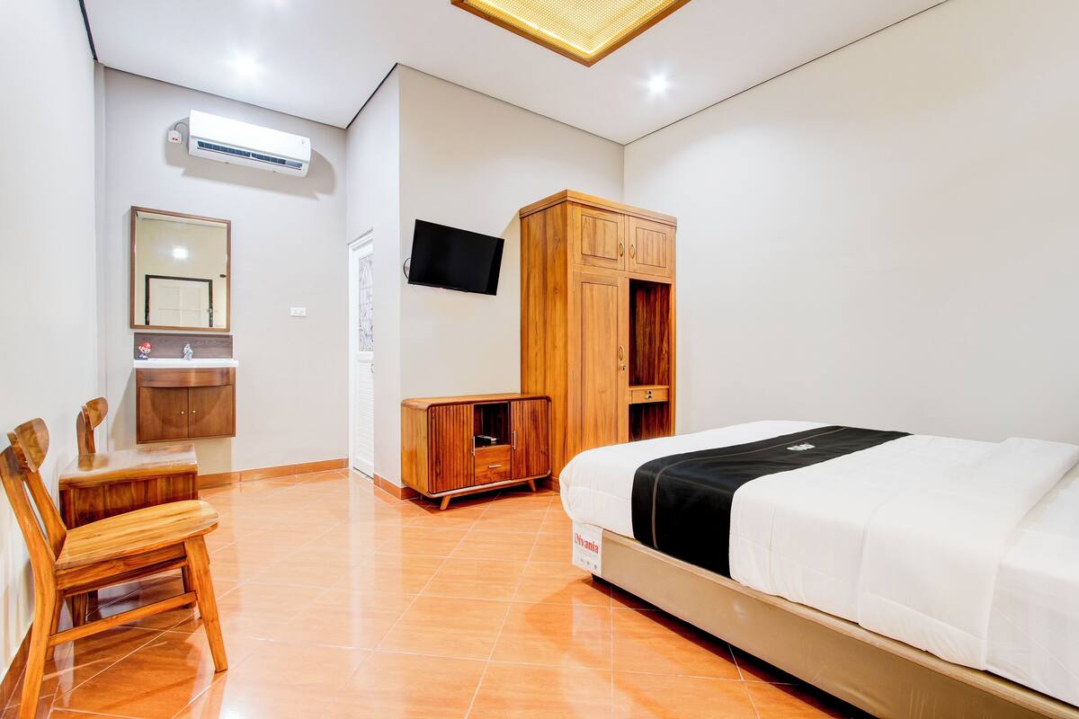 A hotel room with a bed, wooden wardrobe, TV, and a small table with chairs.