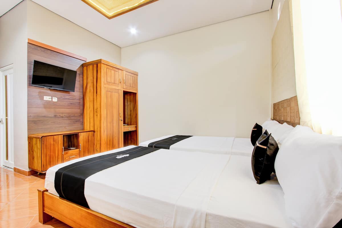 A hotel room with a wooden wardrobe, a television mounted on the wall, and two beds with white bedding.