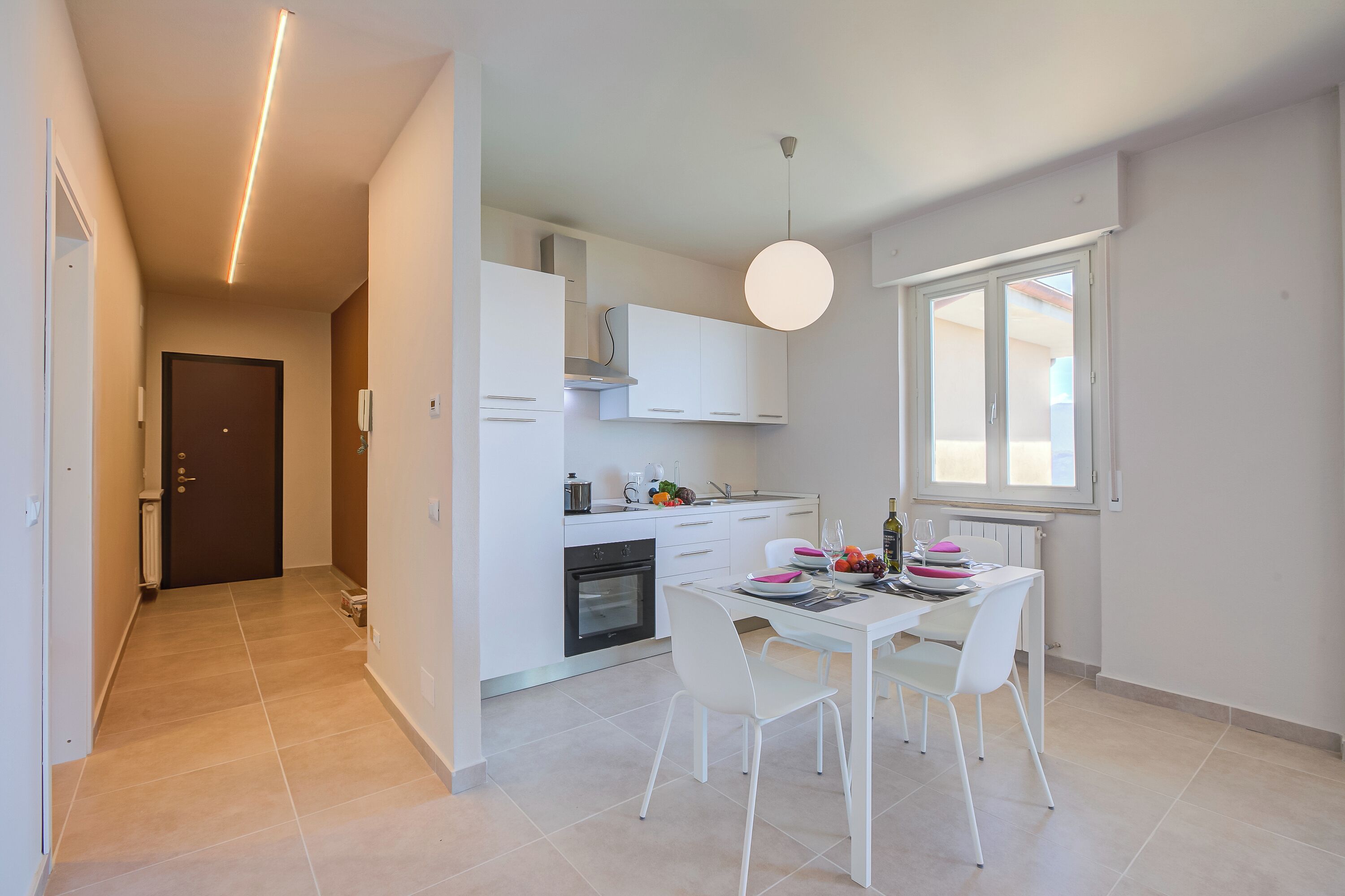 A modern kitchen with white cabinetry, a dining table with chairs, and a pendant light.