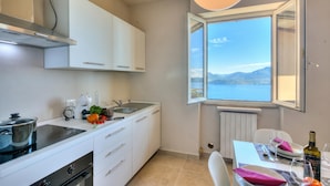 A modern kitchen with white cabinets, a built-in stove, and a window with a view of the sea. - The Golden View: 2-bed Apartment w/ AC (Belgirate)