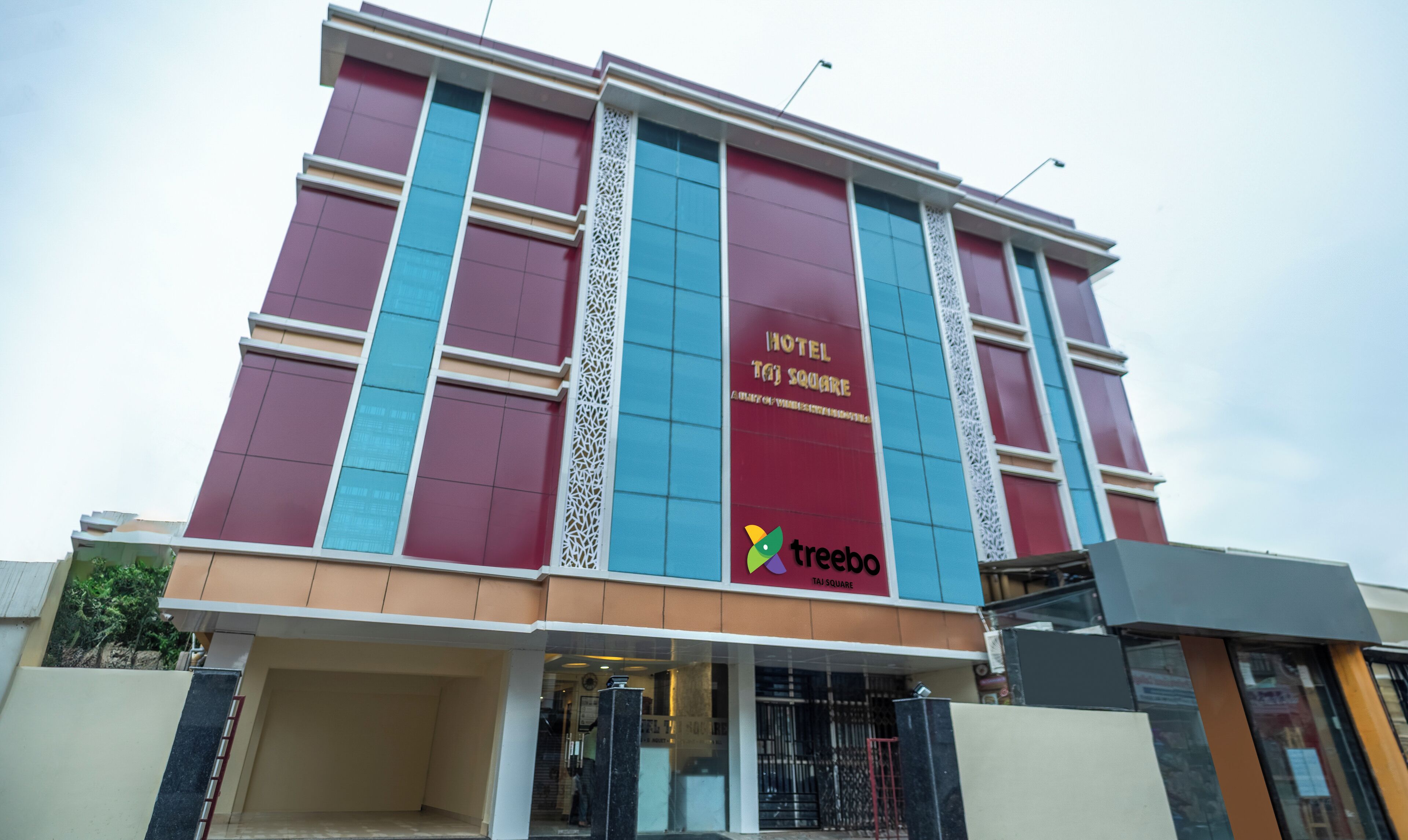 Un edificio moderno con un cartel que dice 'Hotel Taj Square' y un logotipo de 'Treebo'.