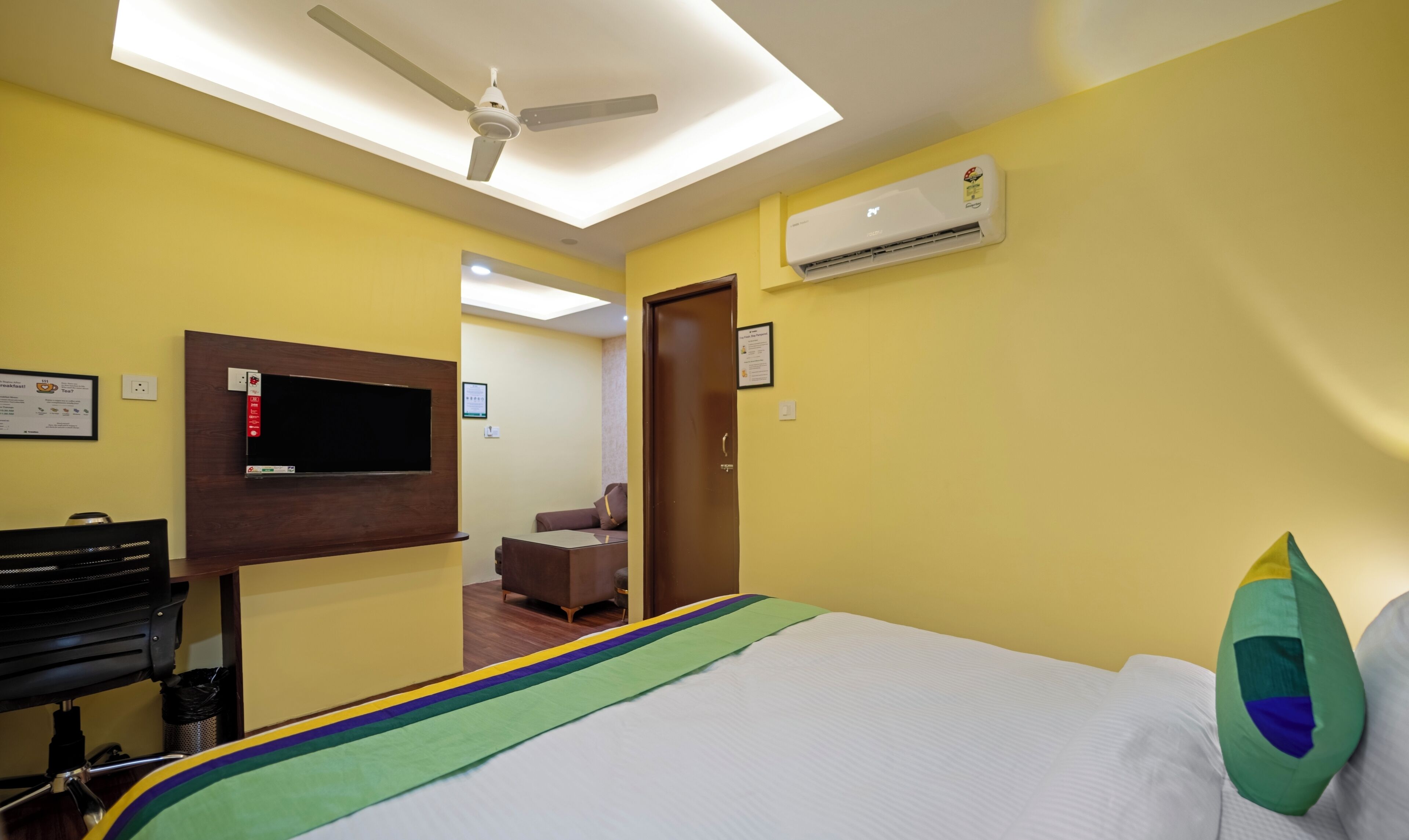A hotel room with a bed, a desk, a chair, a television, and an air conditioning unit.