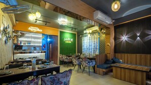 Un ristorante con zona bar, posti a sedere rivestiti di fiori e una parete verde con insegna al neon.