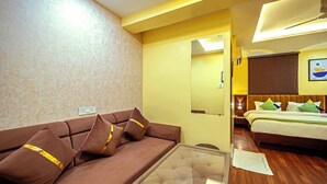 Una camera d'albergo con un divano marrone, un letto con testiera in legno, uno specchio e un quadro appeso al muro.