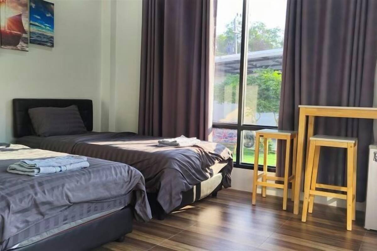 Una habitación con dos camas, una mesa de madera y una ventana con cortinas.