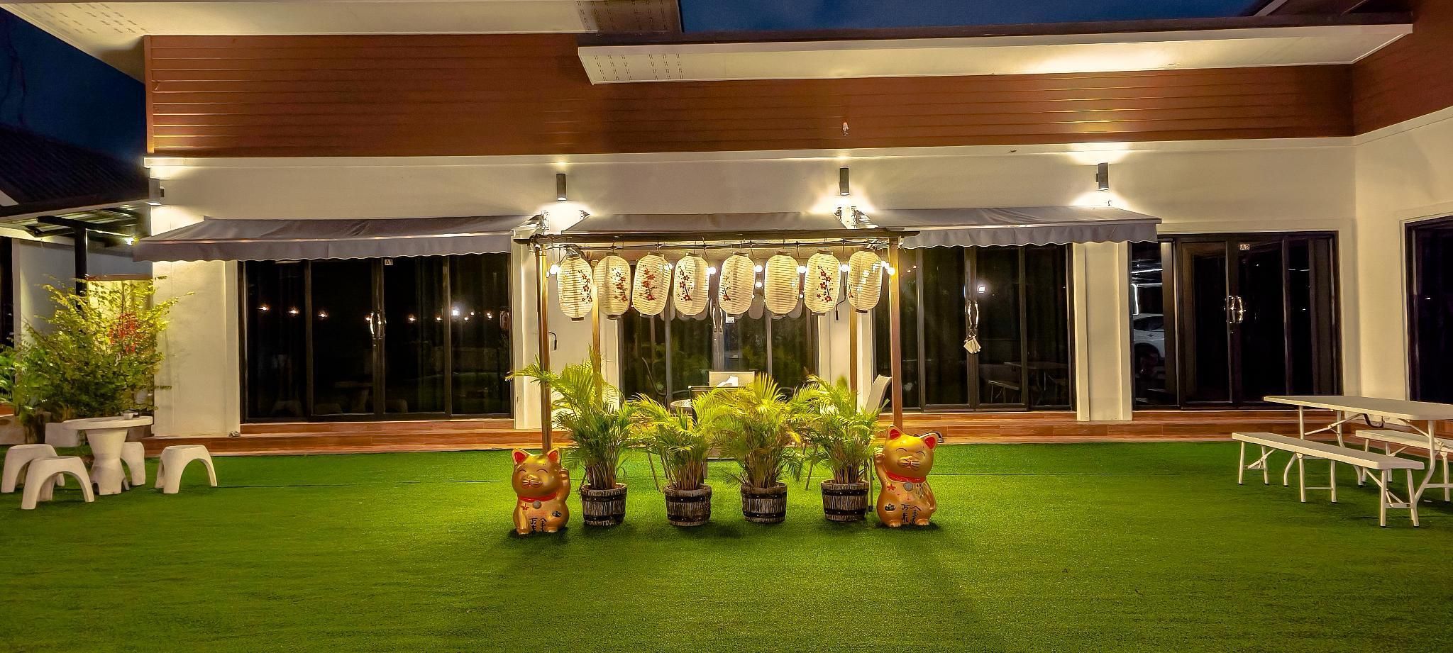 Un área de estar al aire libre con techo, césped artificial, plantas en macetas y un toldo decorativo.