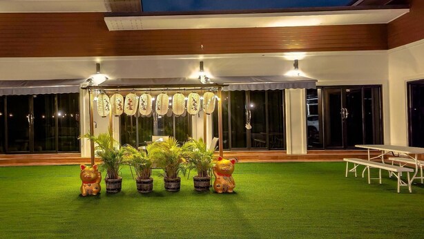 Un área de estar al aire libre con techo, césped artificial, plantas en macetas y un toldo decorativo.