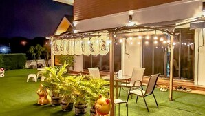 Un edificio moderno con un área de estar al aire libre techada, plantas en macetas y un césped bien cuidado.