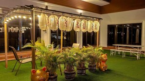 Un patio con una mesa y sillas blancas, una estructura de farol decorativo y plantas en macetas.