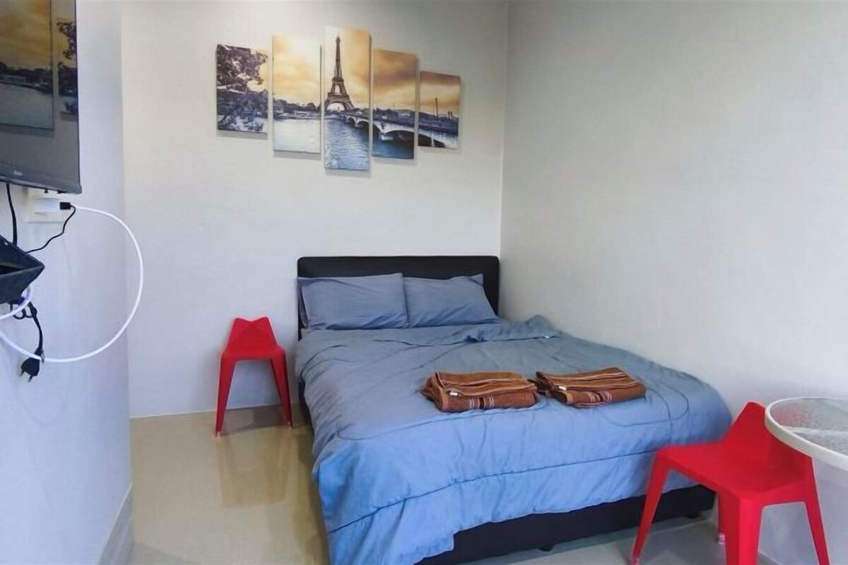 A room with a bed, a red chair, a small table, and wall art depicting the Eiffel Tower.