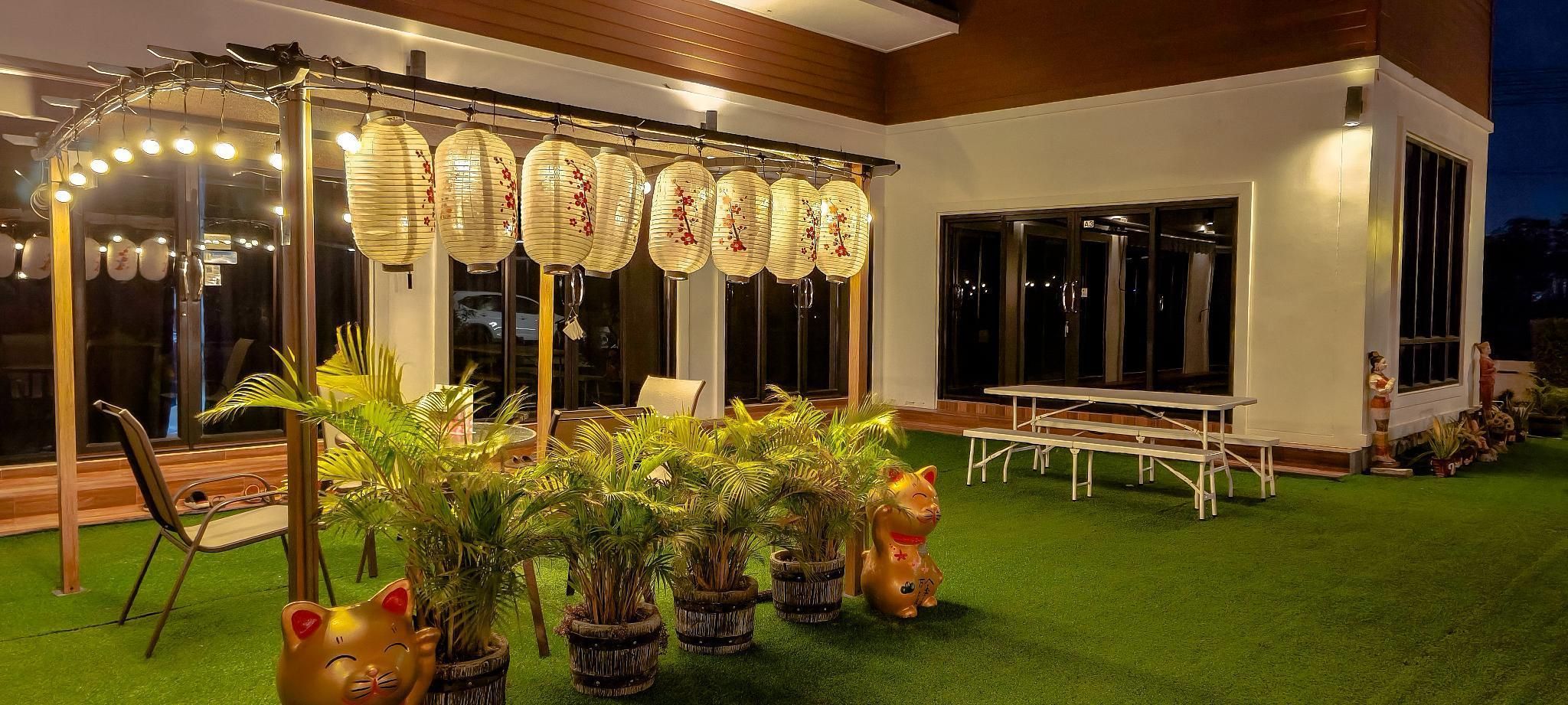 Un patio con una mesa y sillas blancas, una estructura de farol decorativo y plantas en macetas.