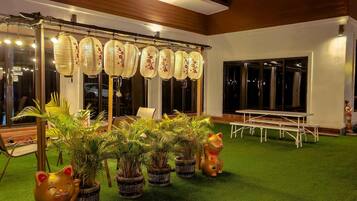 Un patio con una mesa y sillas blancas, una estructura de farol decorativo y plantas en macetas.