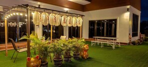Un patio con una mesa y sillas blancas, una estructura de farol decorativo y plantas en macetas.