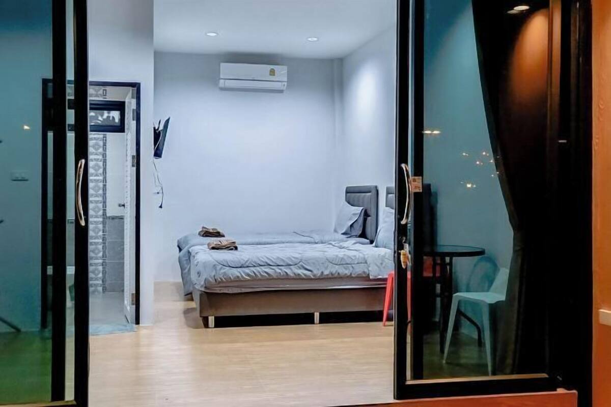 Un dormitorio con cama, una silla, una mesita y un equipo de aire acondicionado.