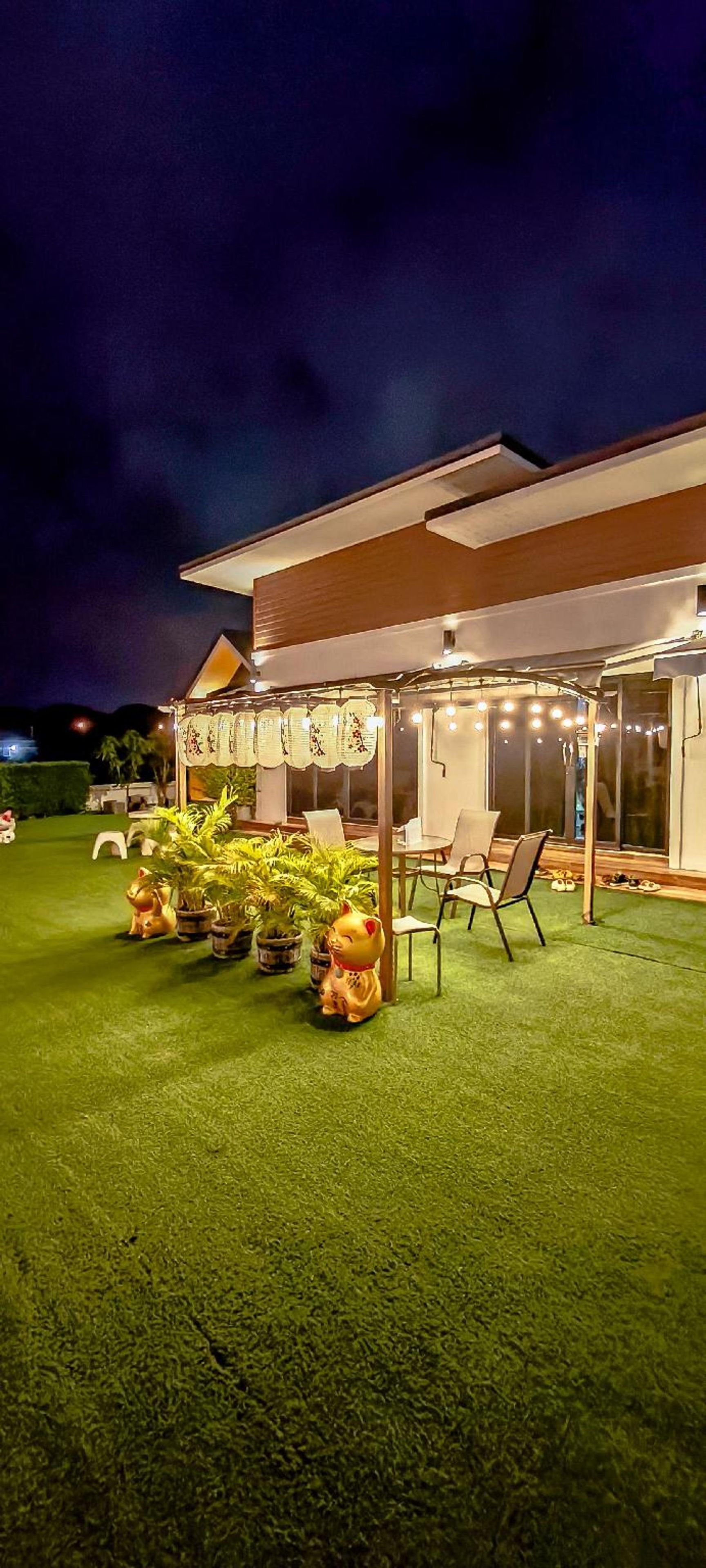 Un edificio moderno con un área de estar al aire libre techada, plantas en macetas y un césped bien cuidado.