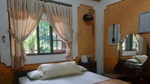 A bedroom with a bed, a nightstand, a mirror, and a window with curtains. - Hotel O Omah Citra Genia Homestay (Ngaglik)