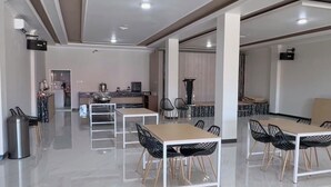 Un comedor amplio y moderno con varias mesas y sillas, una cocina al fondo y un techo alto con iluminación empotrada.