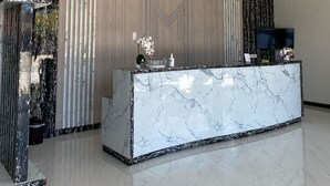 Una moderna recepción con mostrador de mármol, techo decorativo y un amplio ventanal con cortinas.
