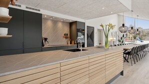 Une cuisine moderne dotée d’un grand îlot central, de meubles de rangement aux couleurs sombres et offrant une vue sur l’extérieur.