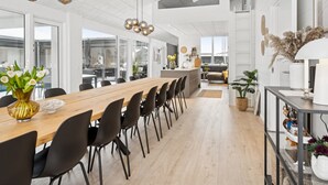 Une cuisine moderne avec une longue table en bois, des chaises noires et des luminaires suspendus.