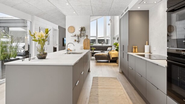 Une cuisine moderne dotée d’un îlot central, d’appareils électroménagers intégrés et offrant une vue sur l’extérieur.