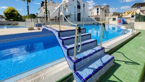 Ein Swimmingpool mit blauen, gefliesten Stufen und einem weißen Gebäude im Hintergrund.